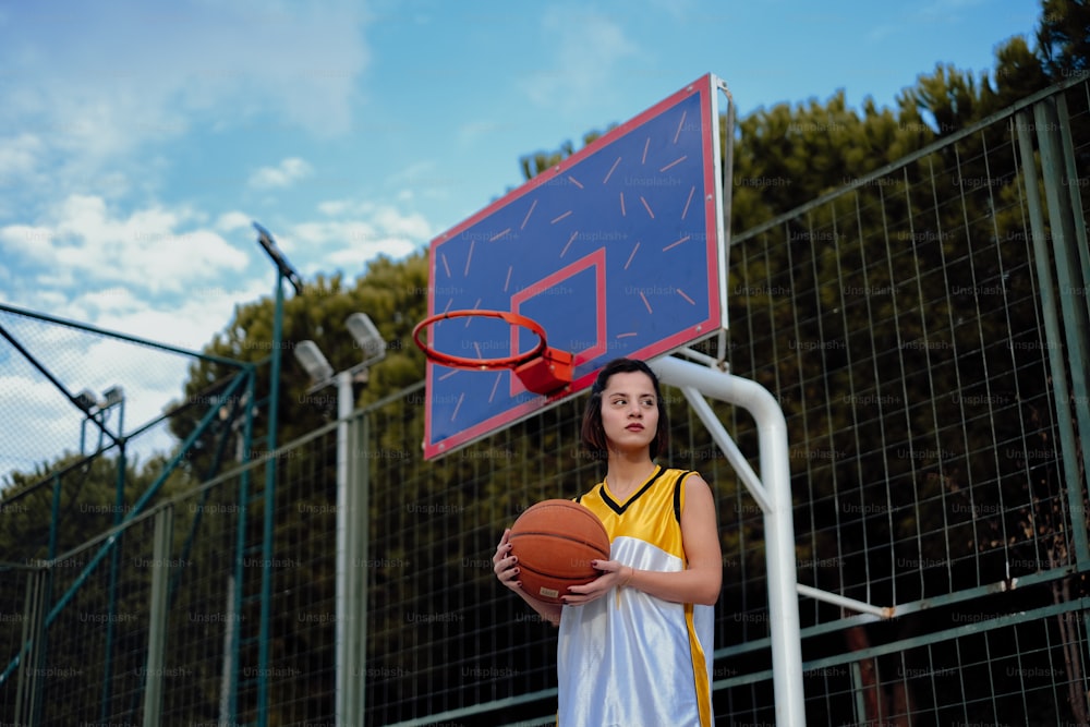 a young girl holding a basketball in front of a basketball hoop