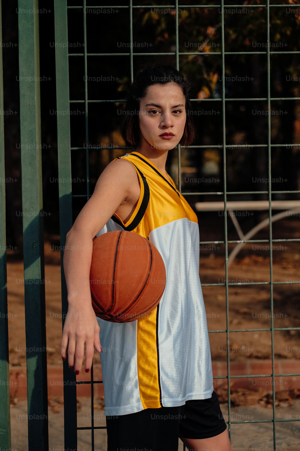 a woman holding a basketball standing next to a fence