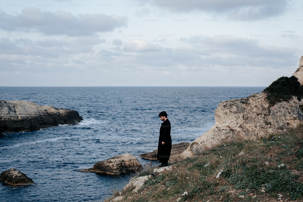 um homem em pé em um penhasco com vista para o oceano