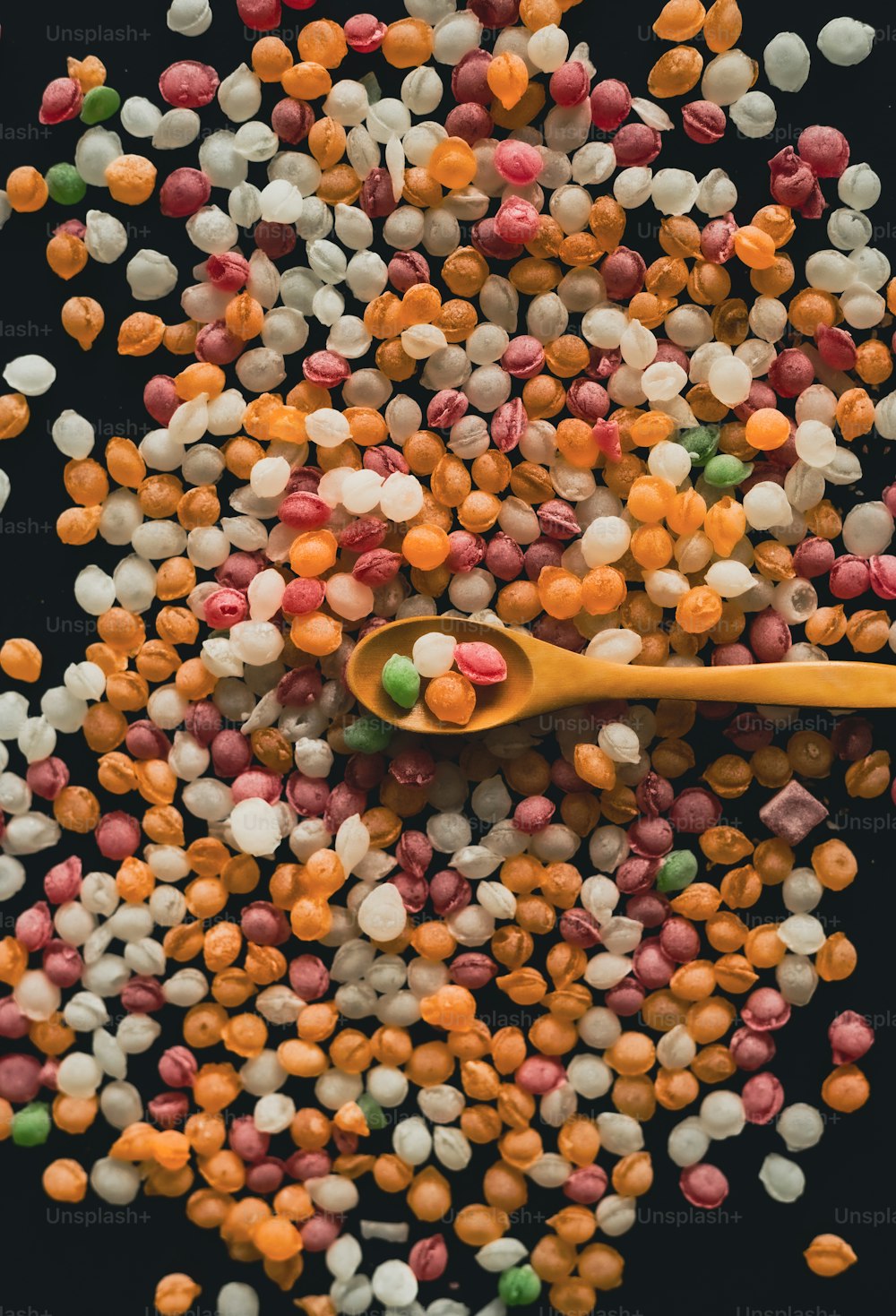 a spoon full of colorful candies on a black surface