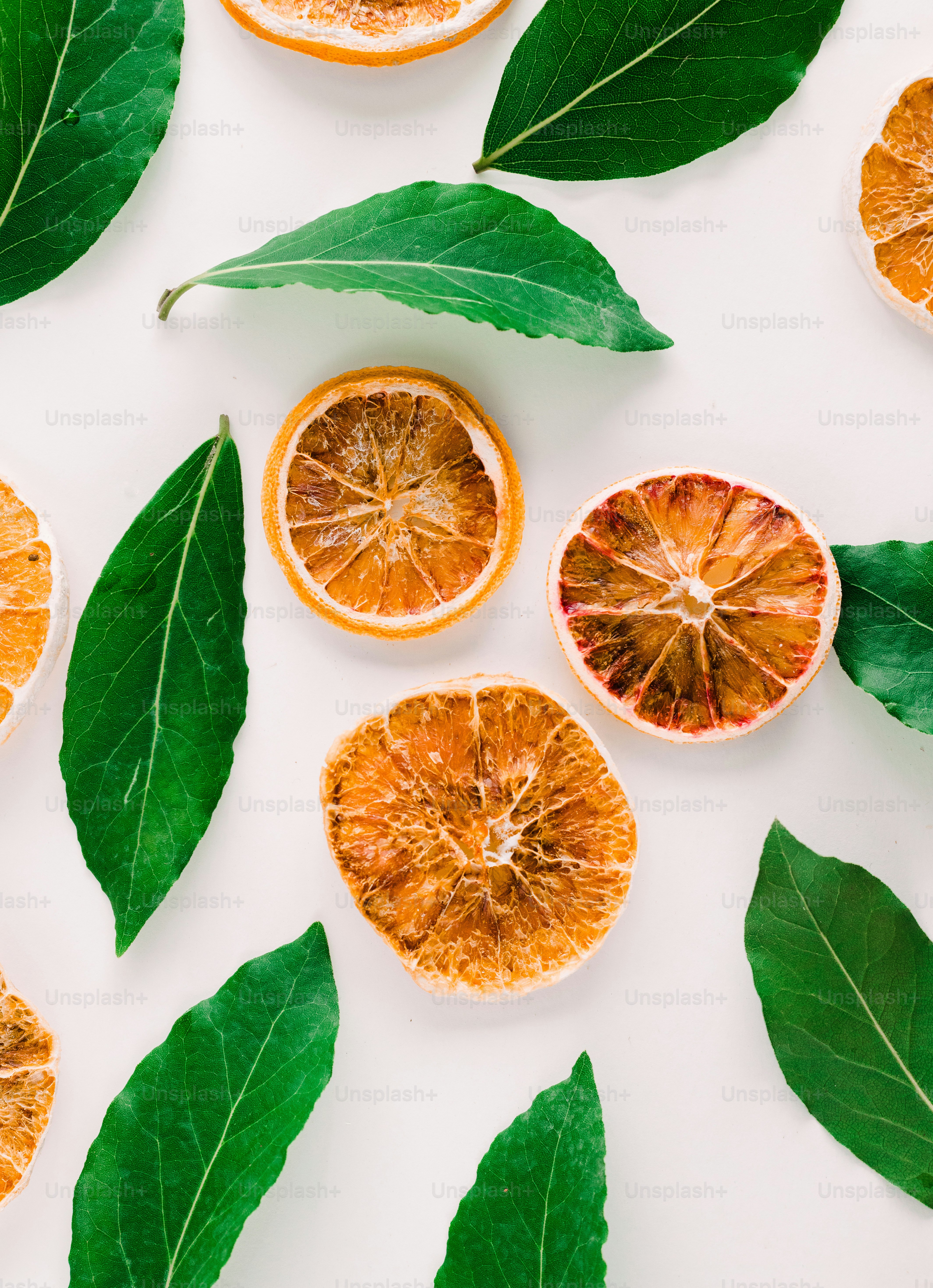 a group of oranges with leaves on a white surface