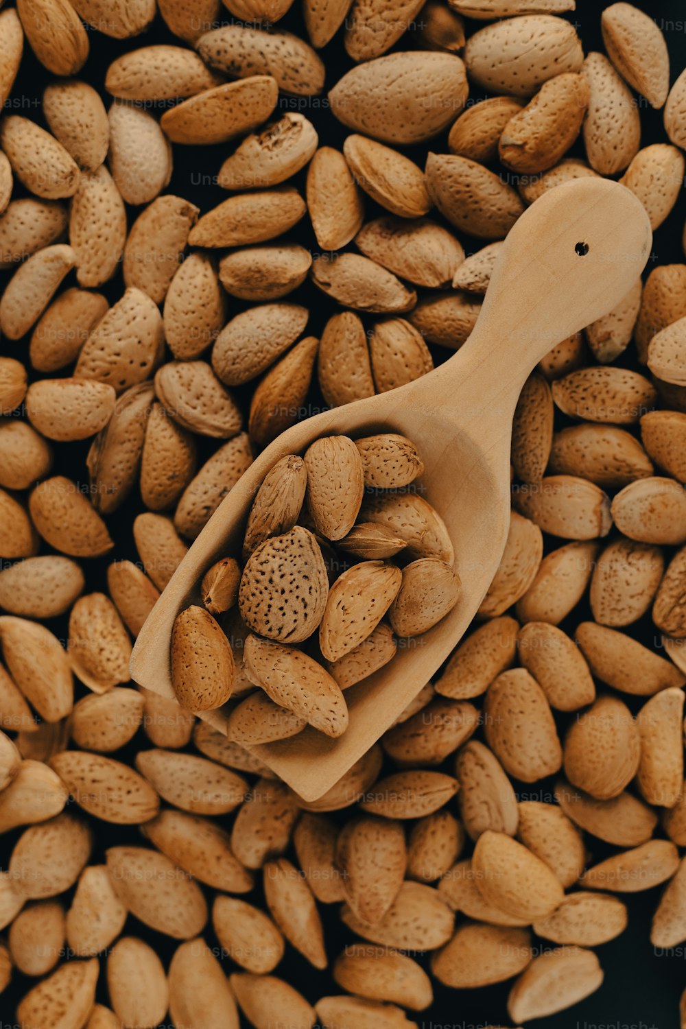 una cuchara de madera llena de cacahuetes encima de una pila de cacahuetes