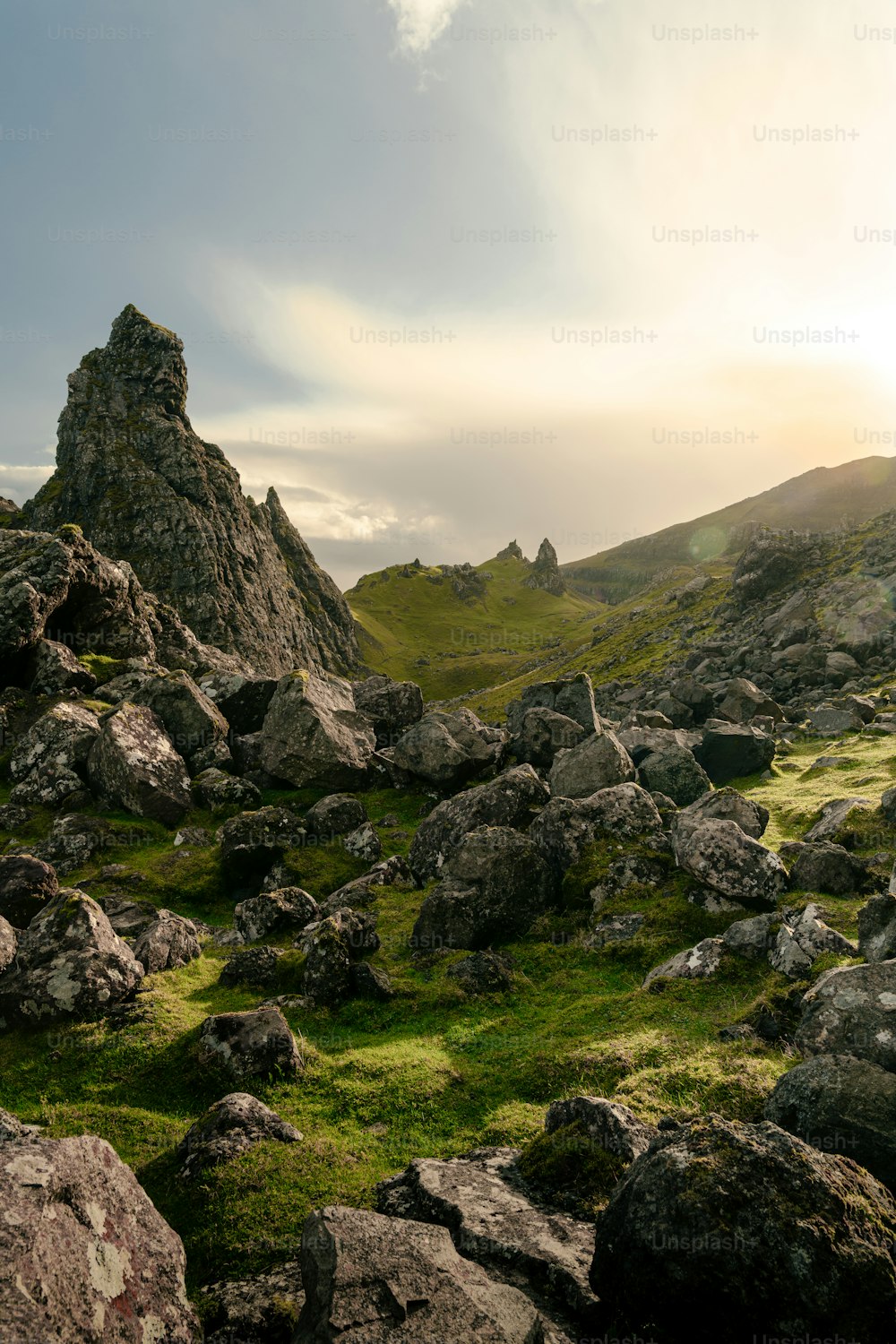 a rocky field with grass and rocks under a cloudy sky