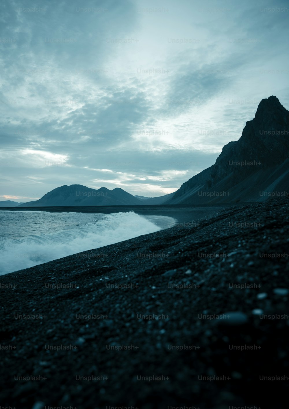 uma praia preta com uma montanha no fundo