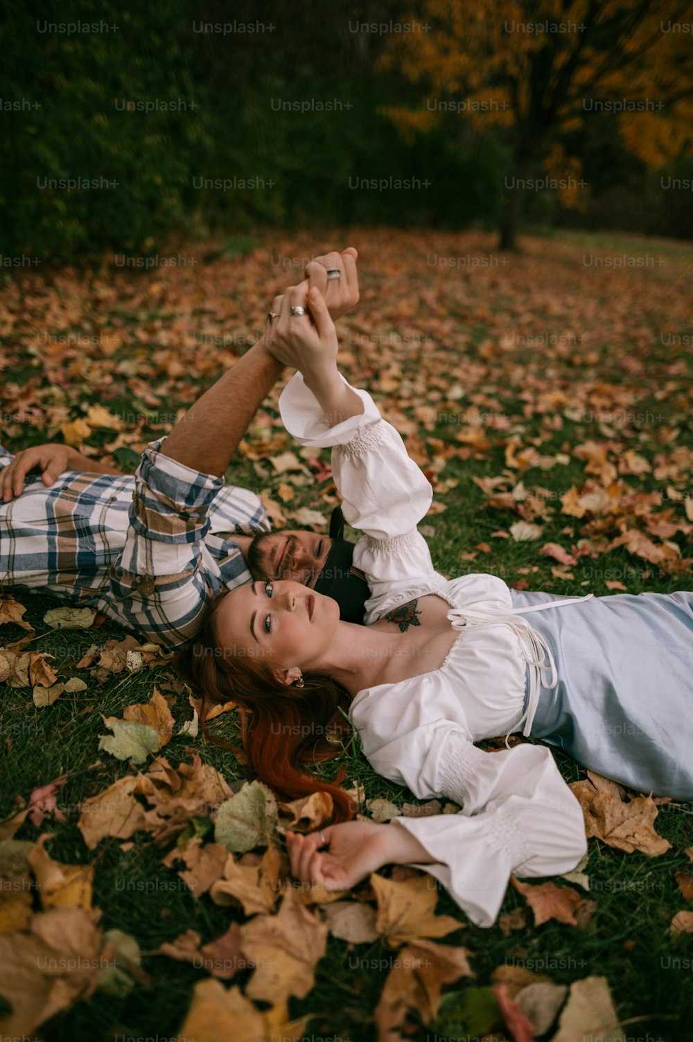 a man and a woman laying on the ground in leaves