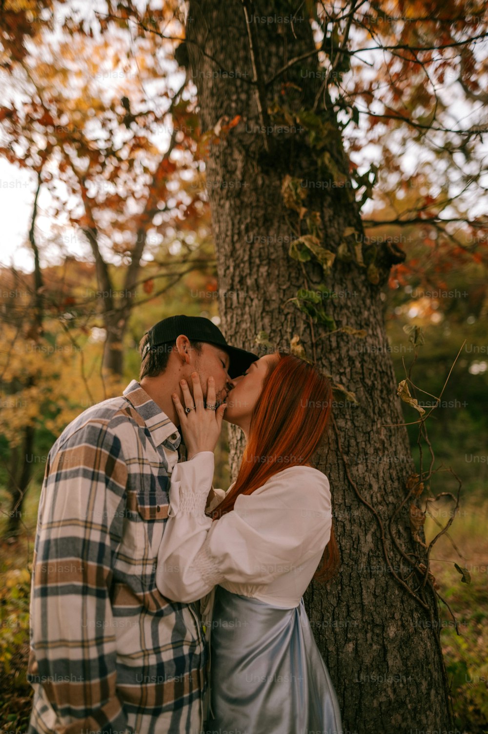 a man and a woman kissing in front of a tree