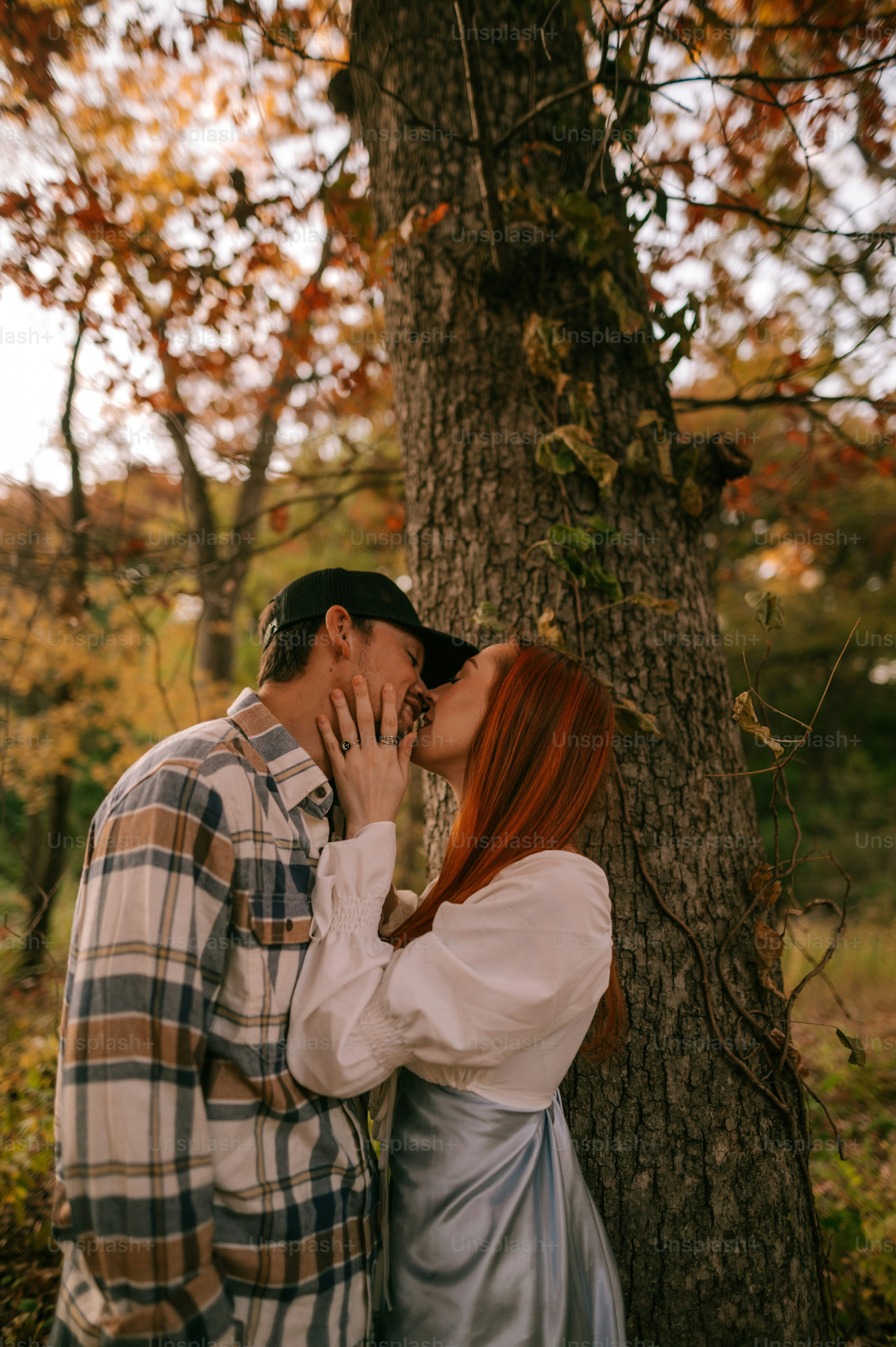 a man and a woman kissing in front of a tree