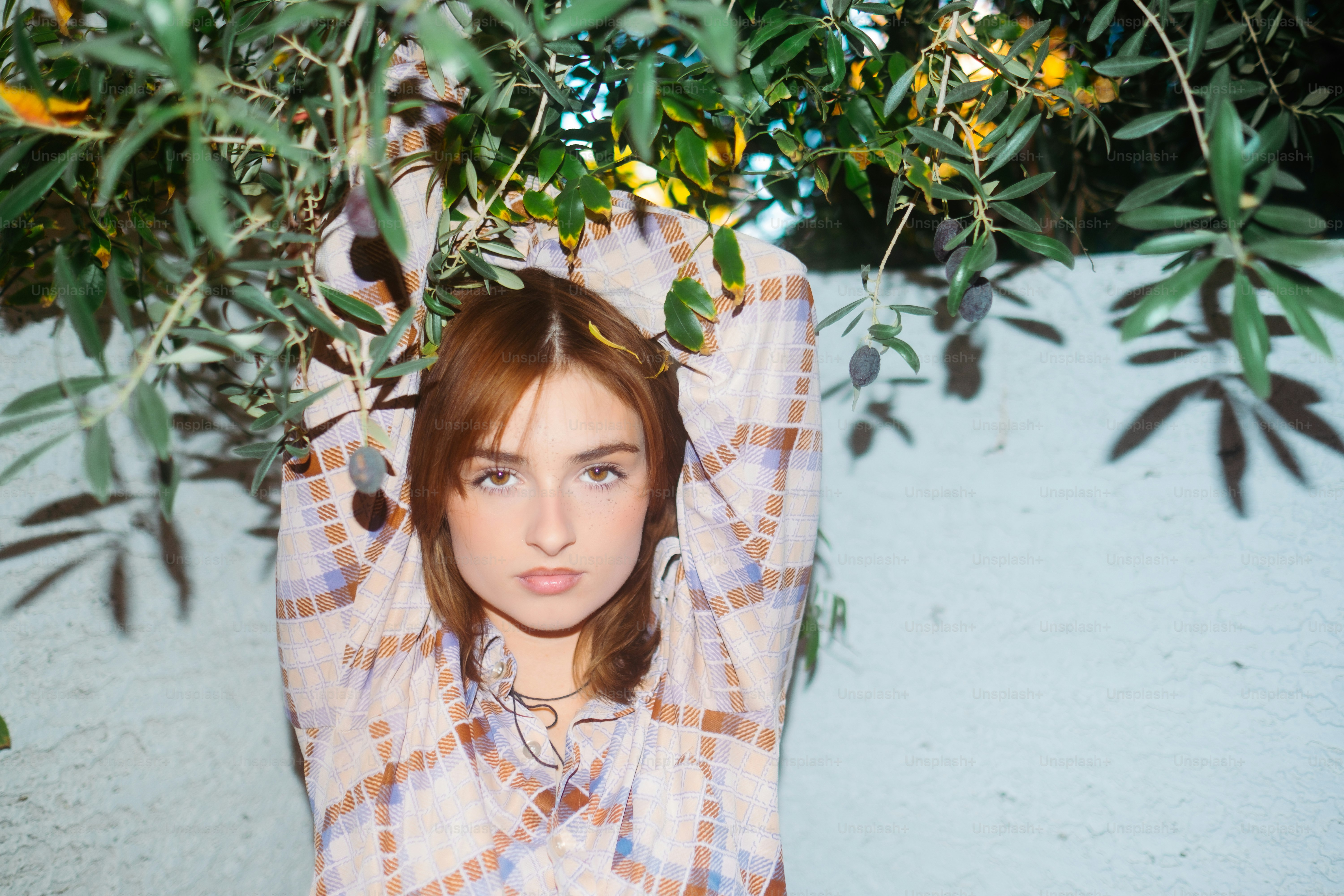 a woman is posing under a tree with her hands on her head