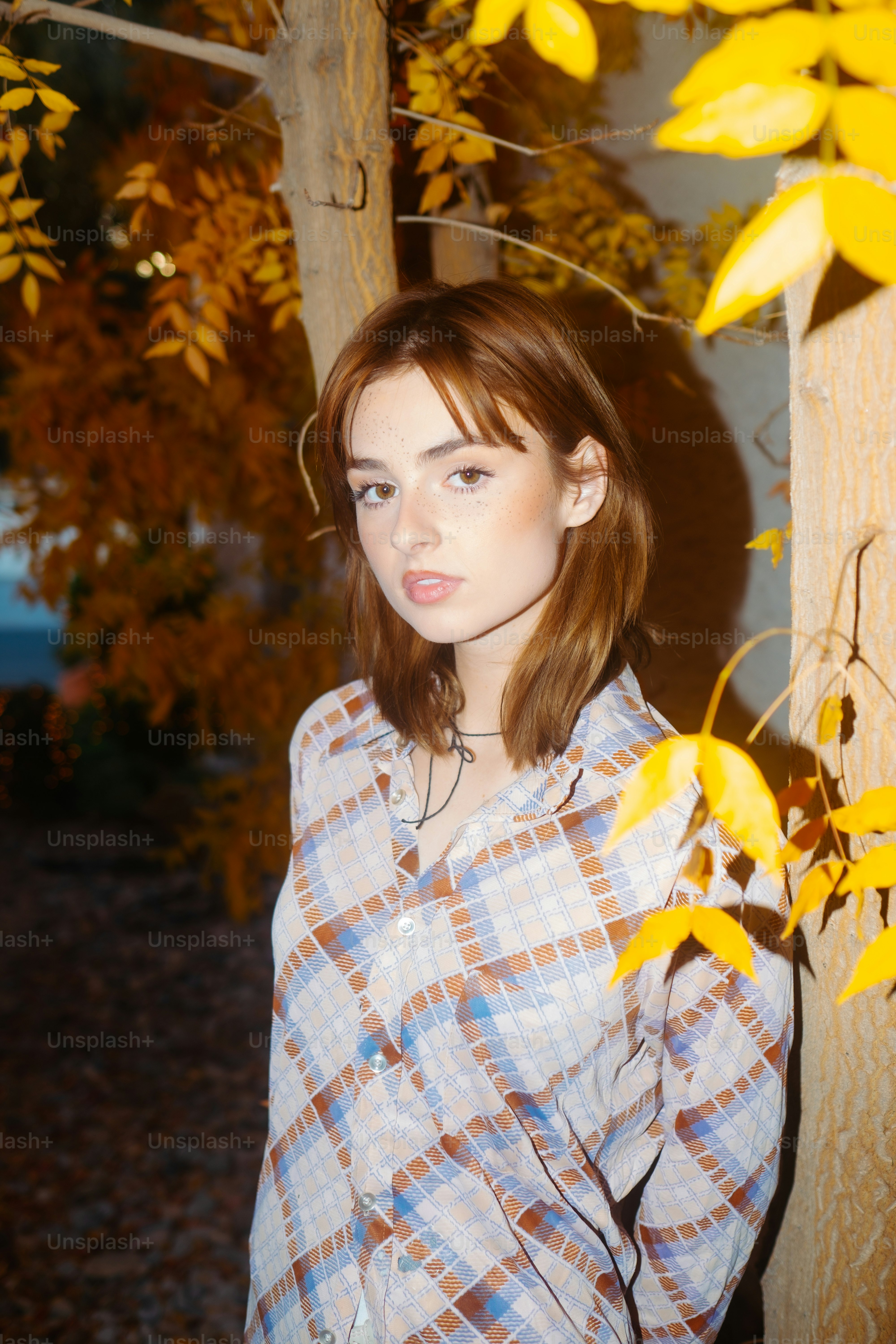 Una mujer de pie junto a un árbol con hojas amarillas