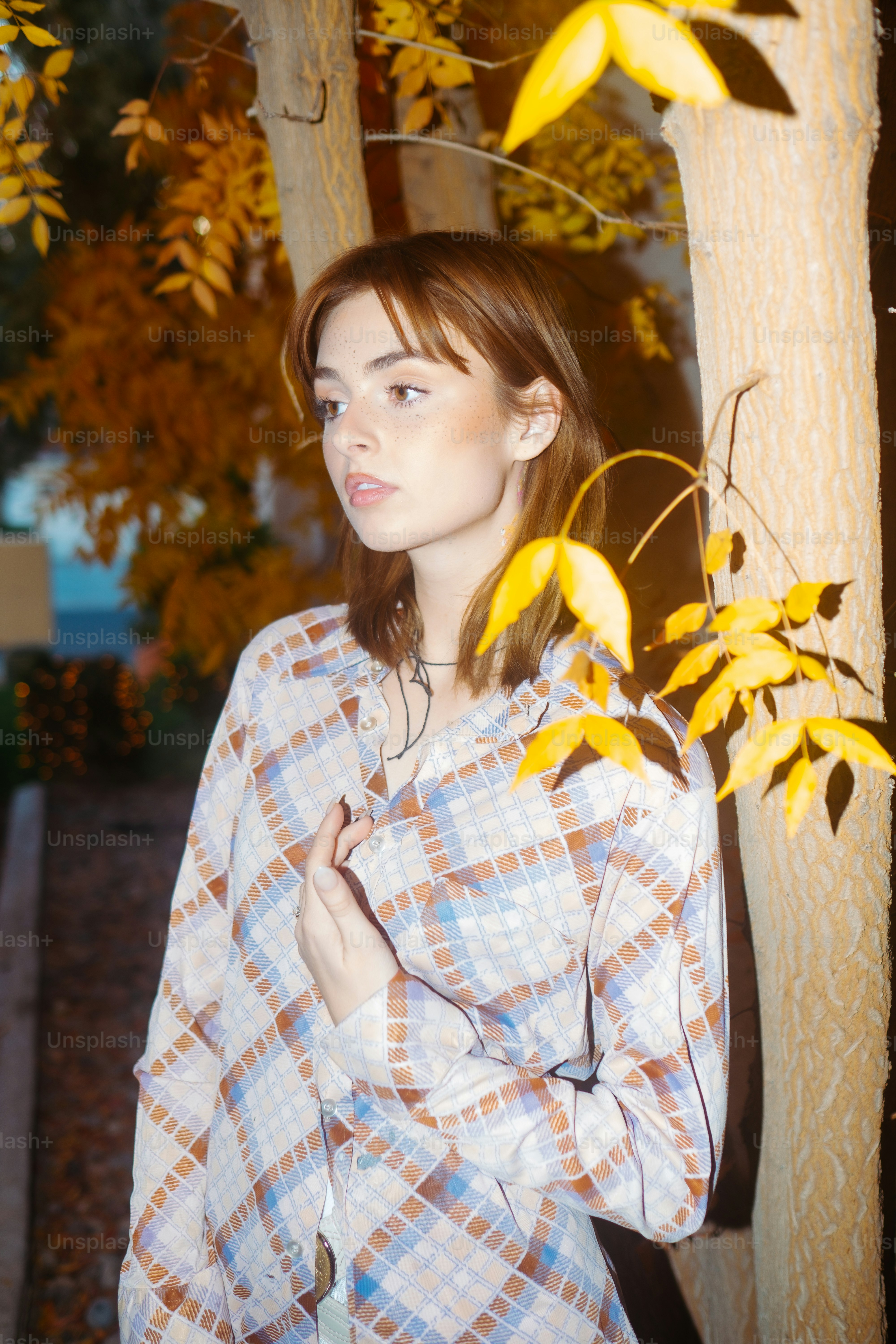 a woman standing next to a tree with yellow leaves