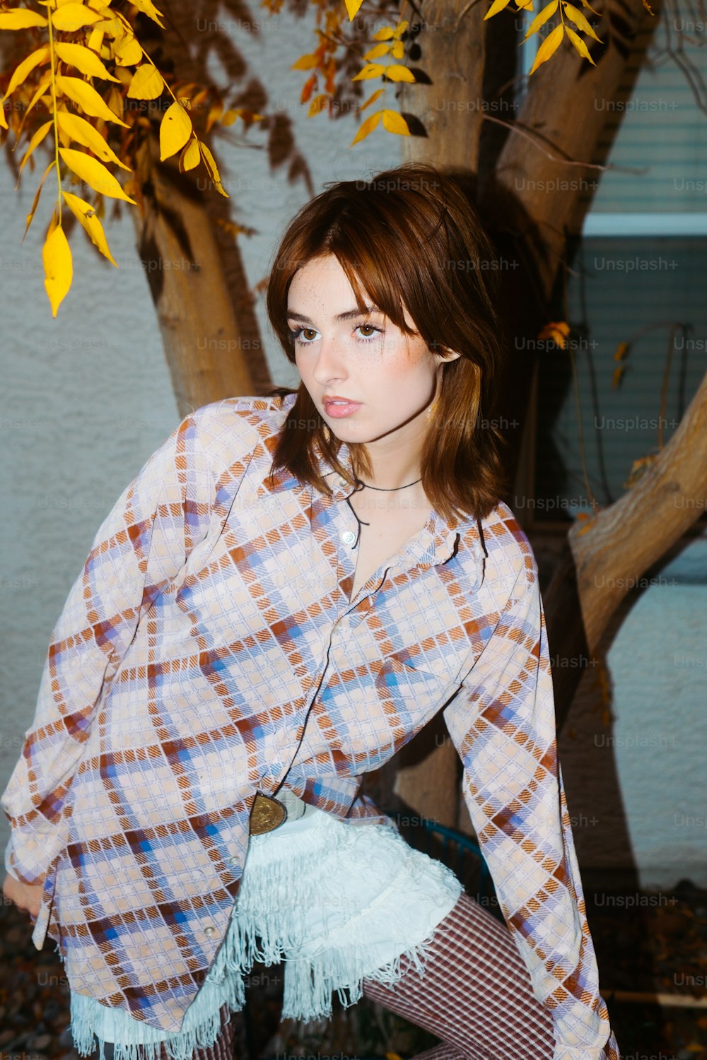 a woman in a plaid shirt leaning against a tree