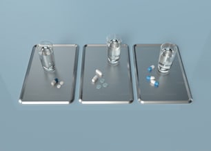 three metal trays with pills and a glass of water