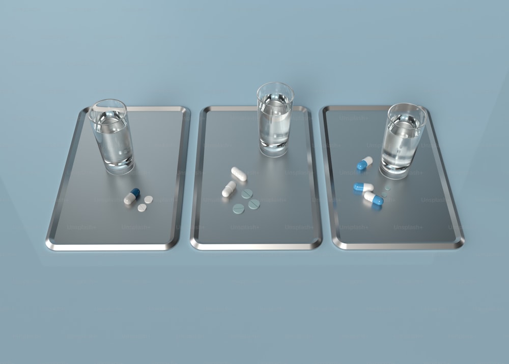 Trois plateaux métalliques avec des pilules et un verre d’eau