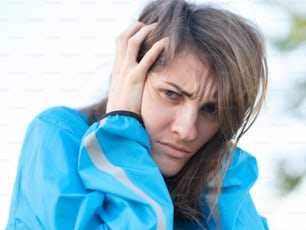 a woman in a blue jacket holding her hand to her head