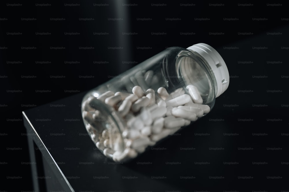 un bocal en verre rempli de pilules blanches assis sur une table