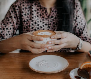 uma mulher sentada em uma mesa segurando uma xícara de café