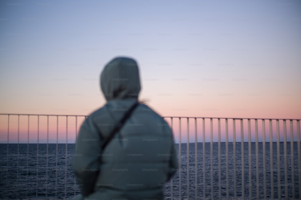 Eine Person, die vor einem Zaun steht und auf das Meer schaut