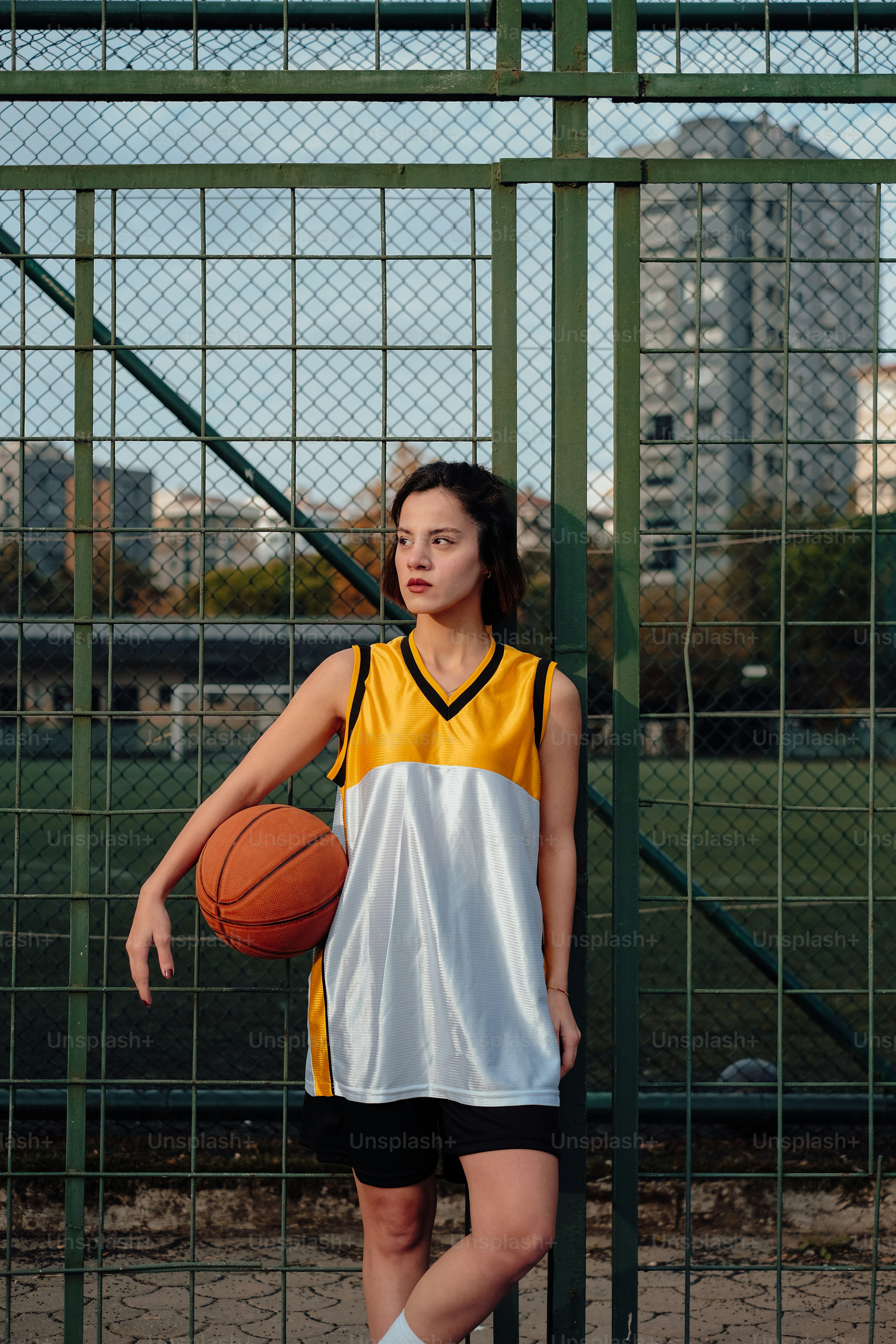 a young woman holding a basketball standing next to a fence
