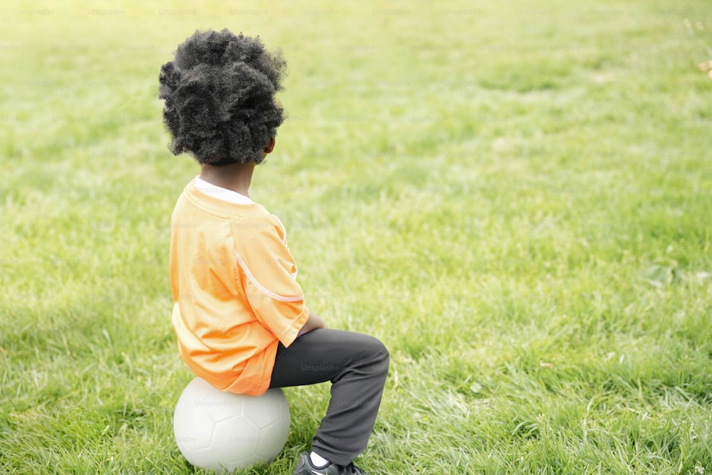 um menino sentado em uma bola na grama