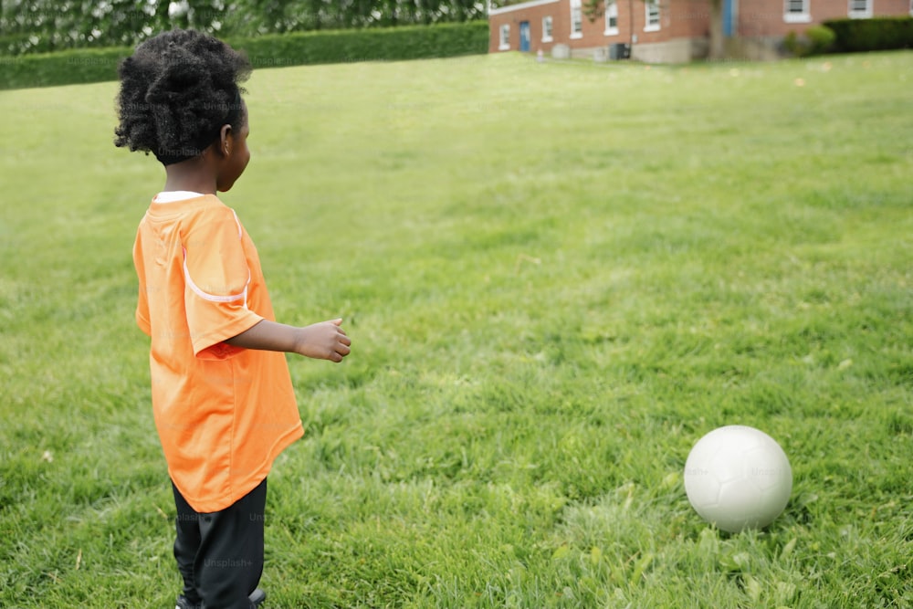 a little boy standing in the grass near a white ball