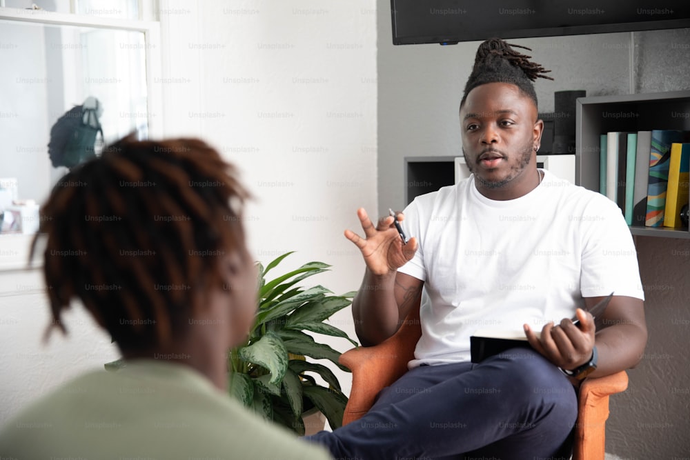 a man sitting in a chair talking to another man