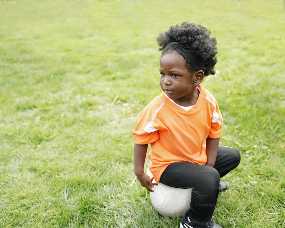 a little girl sitting on top of a soccer ball