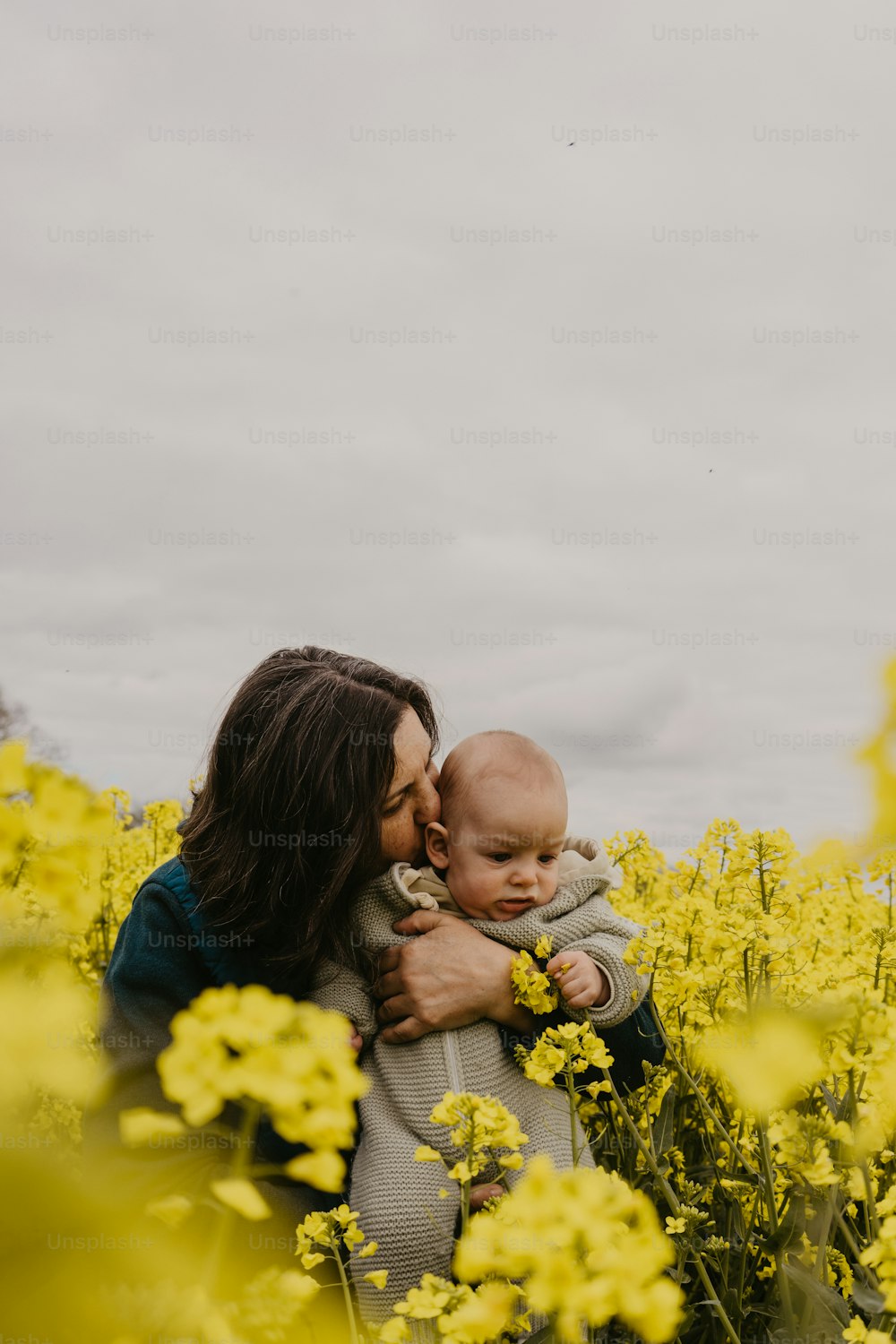 a woman holding a baby in a field of yellow flowers