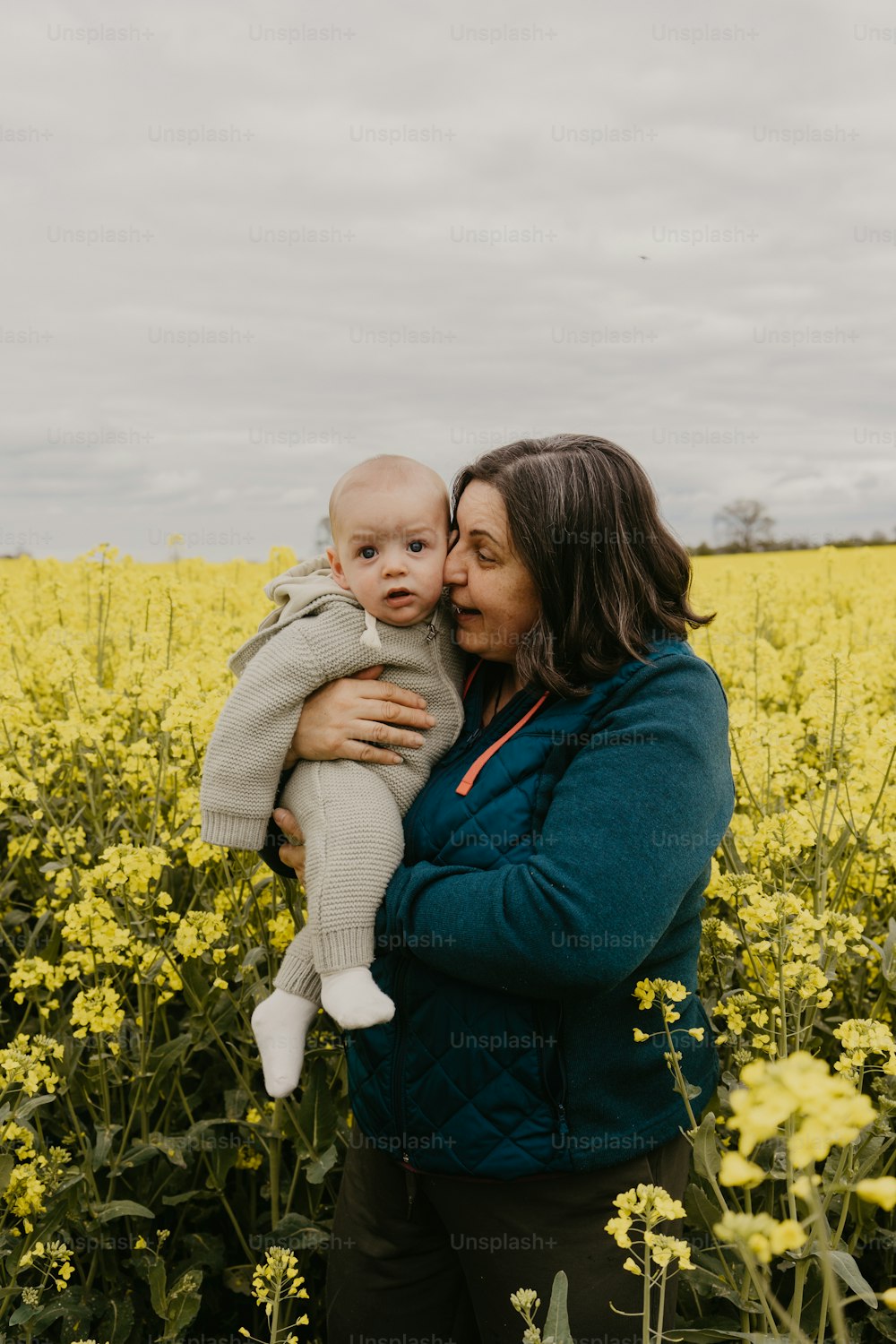 a woman holding a baby in a field of yellow flowers