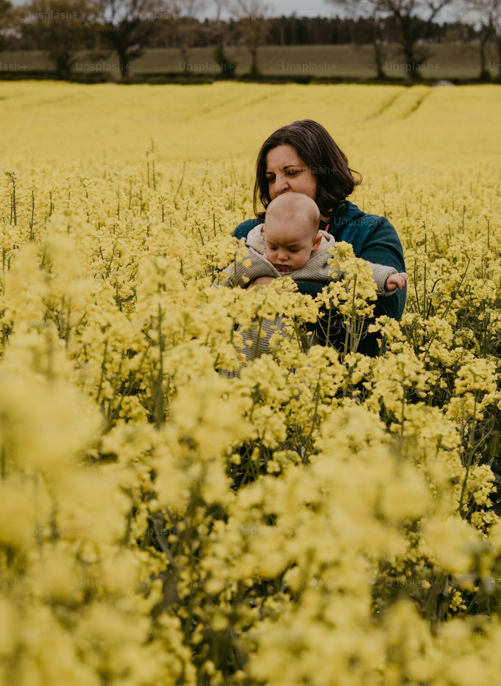 uma mulher segurando um bebê em um campo de flores amarelas