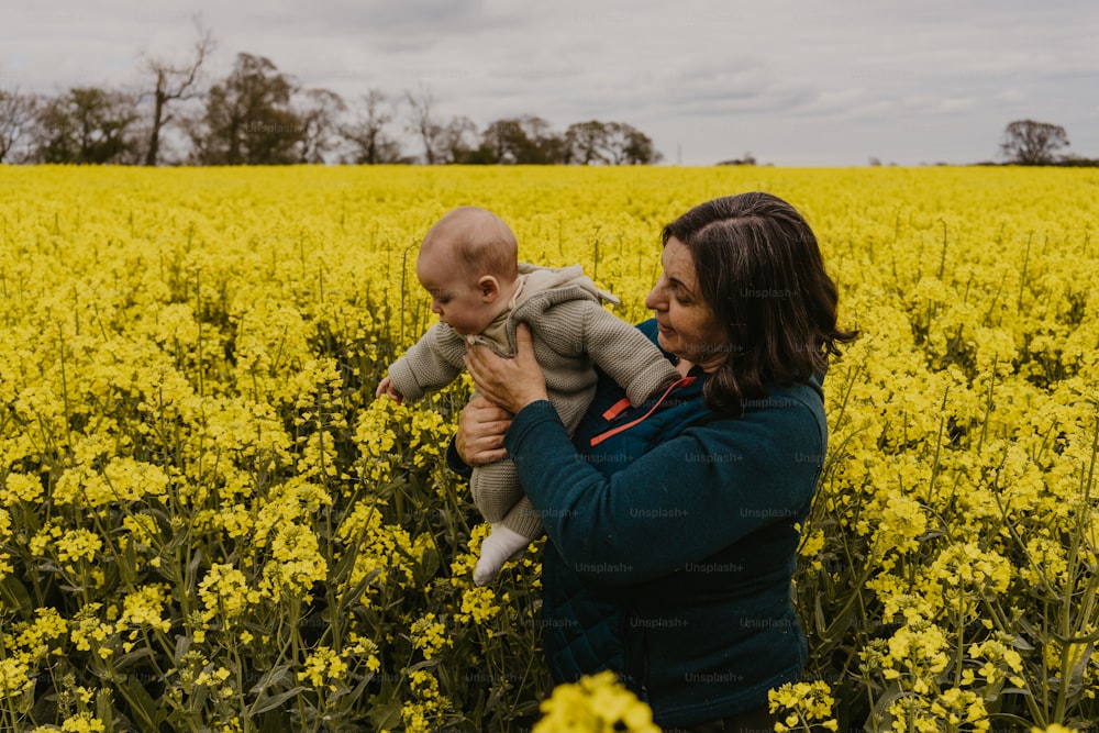 uma mulher segurando um bebê em um campo de flores amarelas
