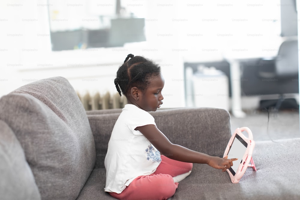 a little girl sitting on a couch playing with a tablet