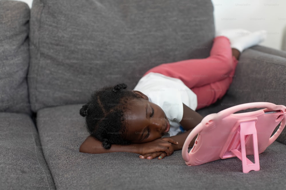 Ein kleines Mädchen, das auf einer Couch neben einer rosa Handtasche liegt