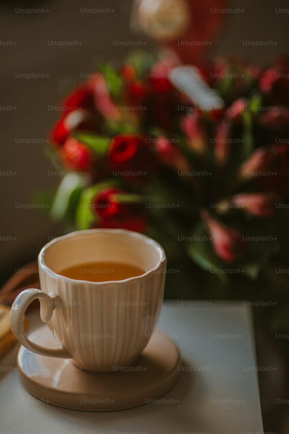 una taza de té en un platillo junto a un jarrón de flores