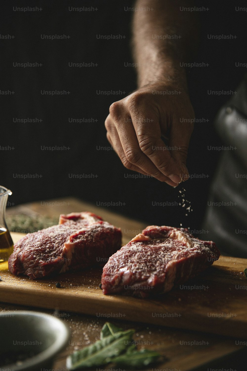 uma pessoa polvilhando tempero em alguma carne em uma tábua de corte