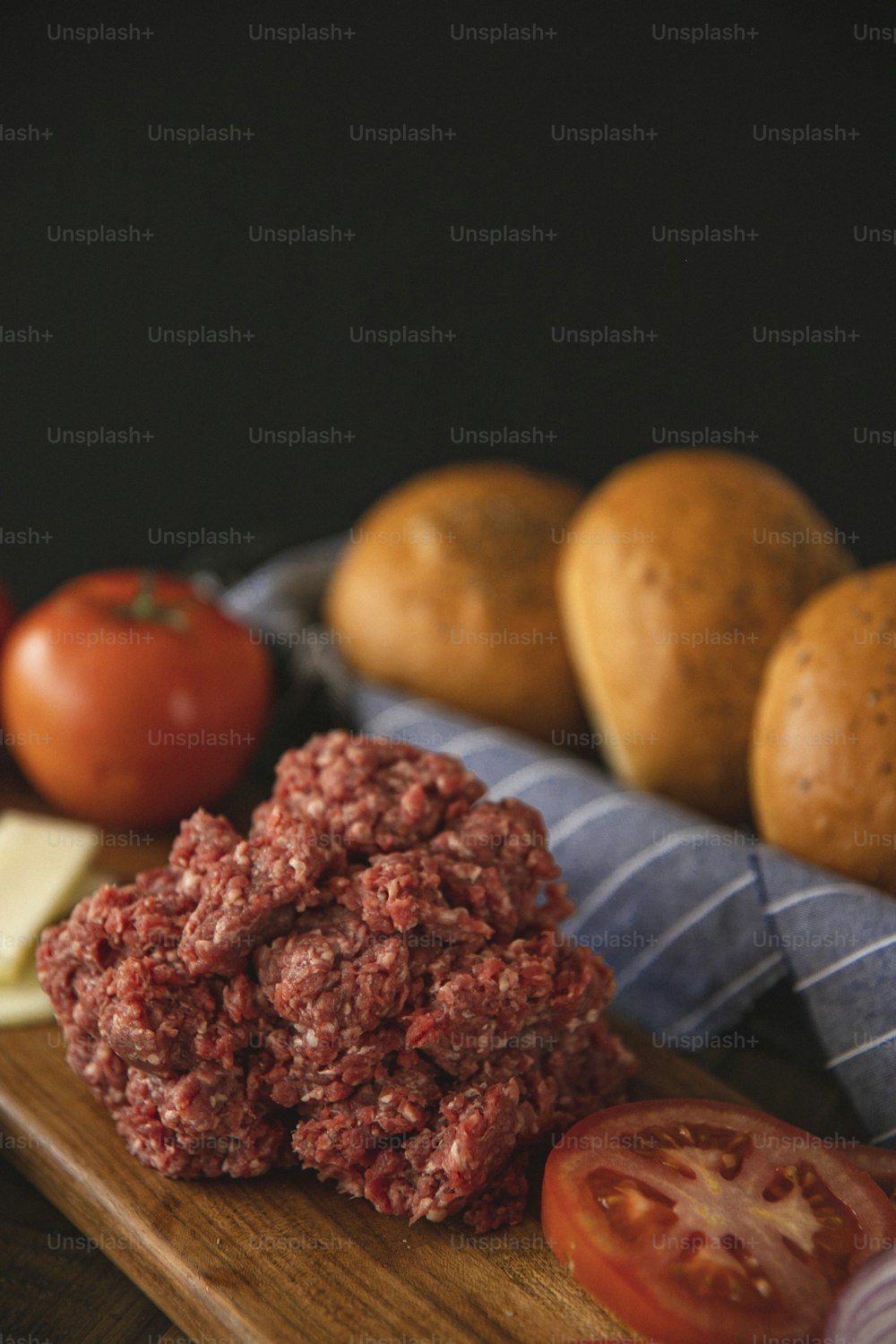 a wooden cutting board topped with hamburger patties and tomatoes