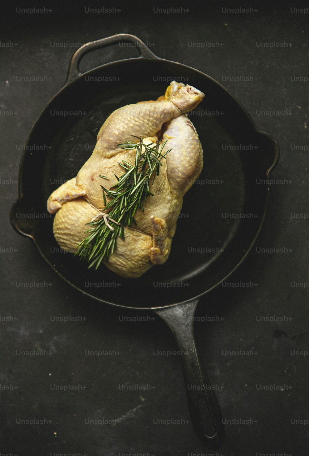 a raw chicken in a cast iron skillet with a sprig of rosemary