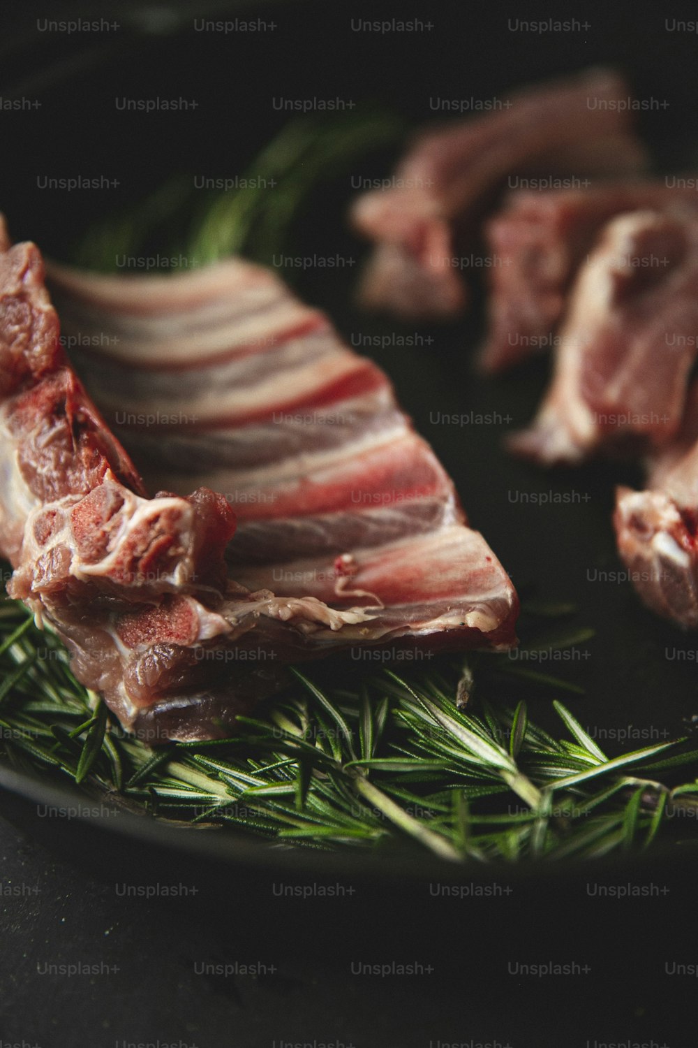 a plate of raw meat with rosemary sprigs