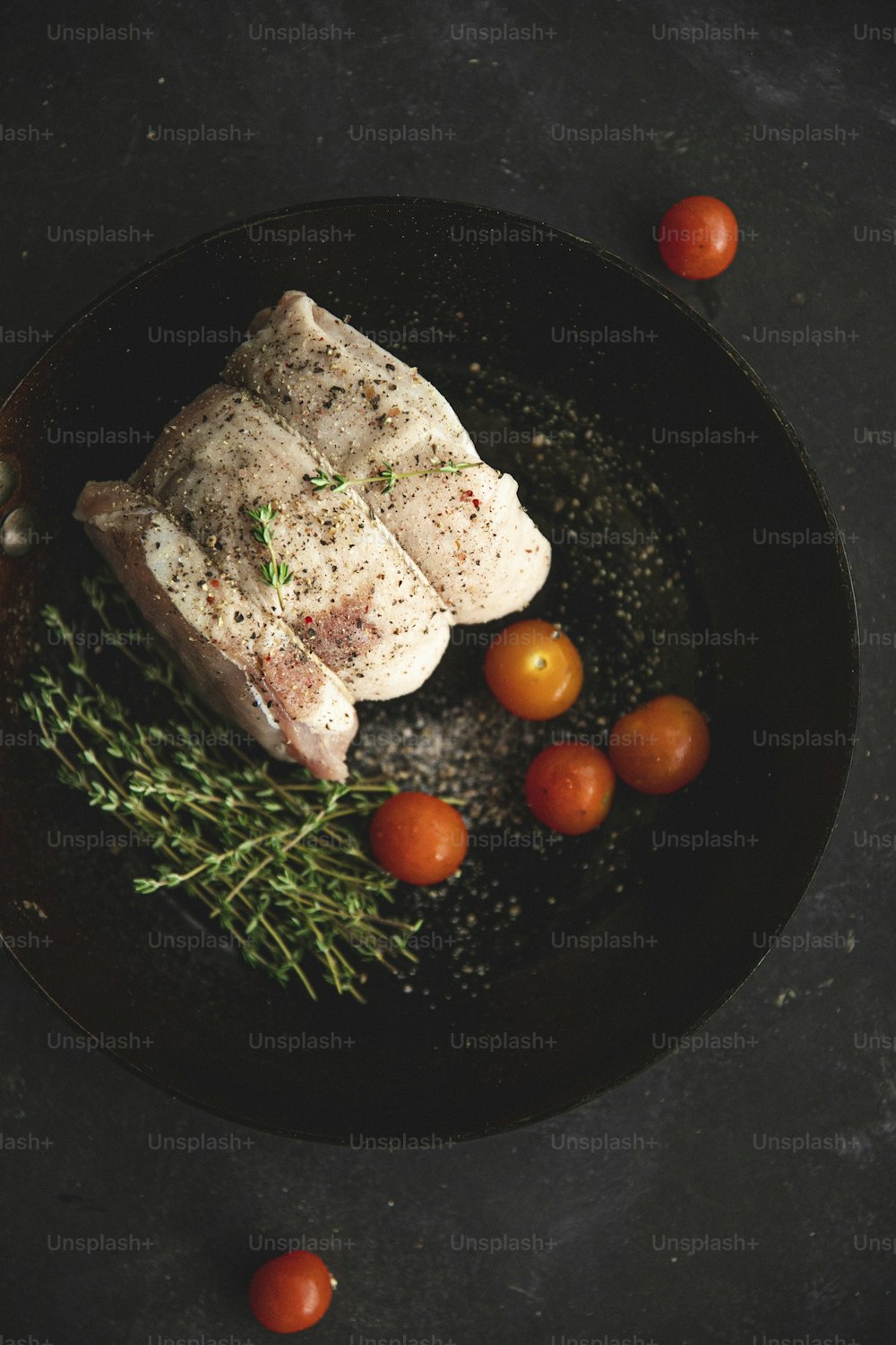 a piece of meat and some tomatoes on a black plate