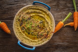 a bowl of hummus and carrots on a wooden table