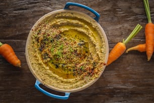 un tazón de hummus y zanahorias sobre una mesa de madera