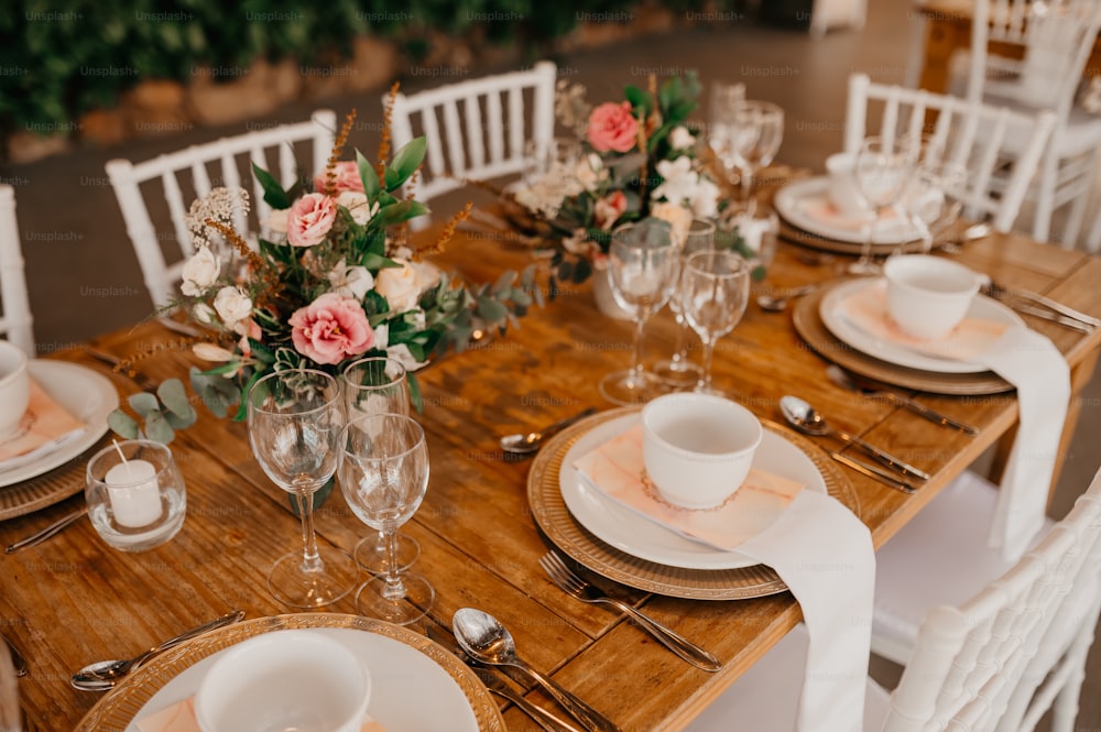 a wooden table topped with white plates and white chairs