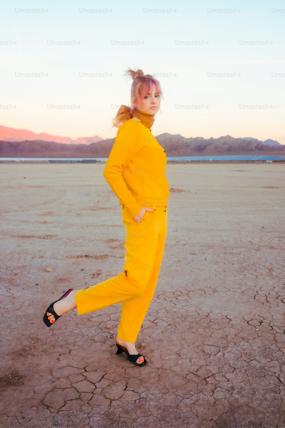 a woman in a yellow jumpsuit standing in a desert
