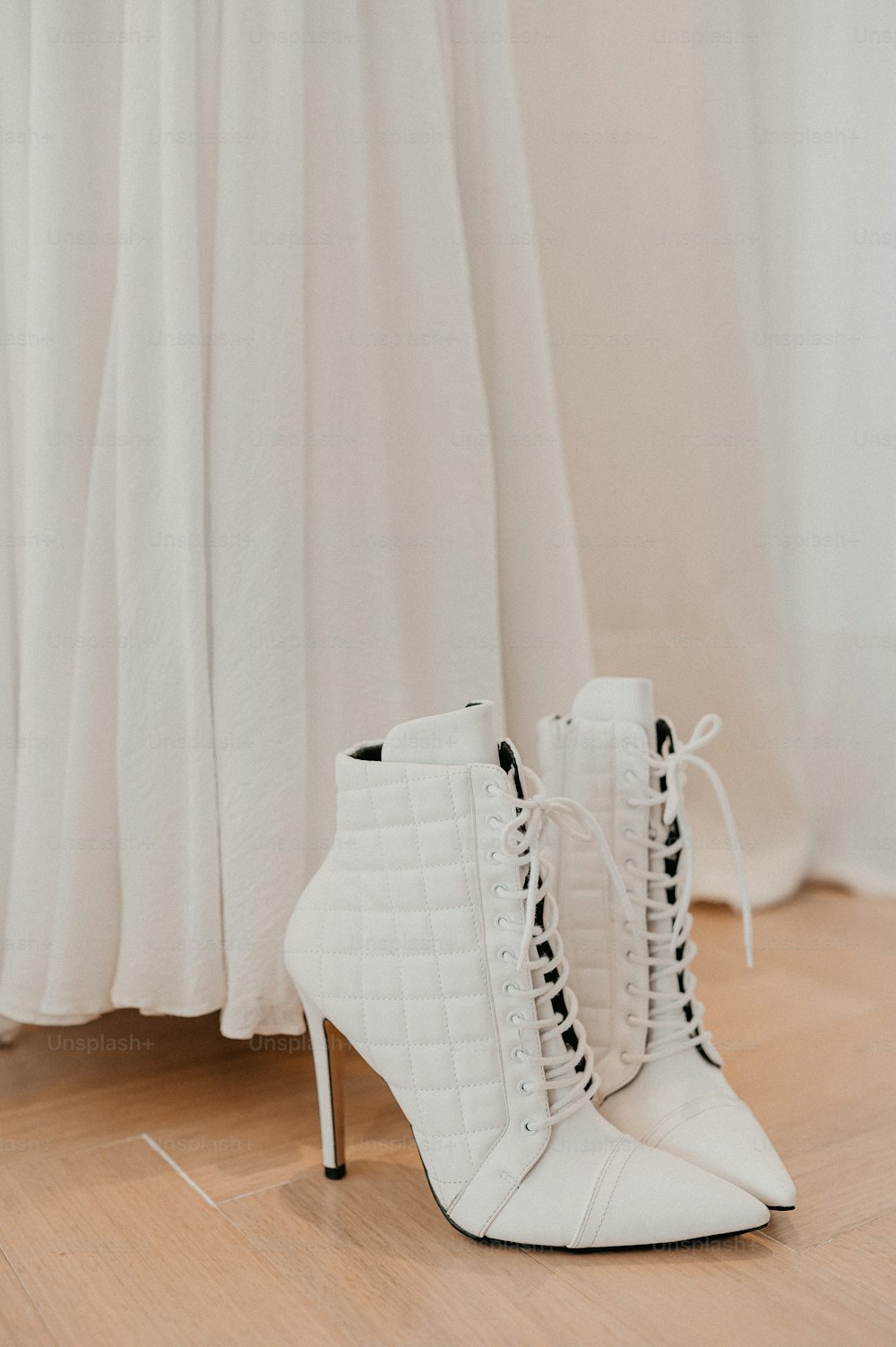 un paio di scarpe bianche con tacco alto sedute sopra un pavimento di legno
