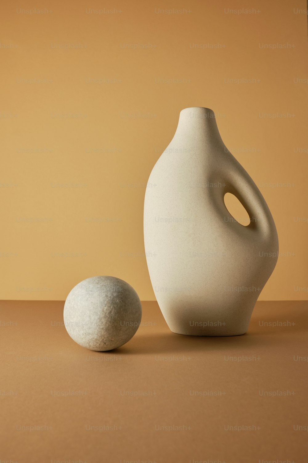 un vase blanc assis à côté d’une boule blanche sur une table
