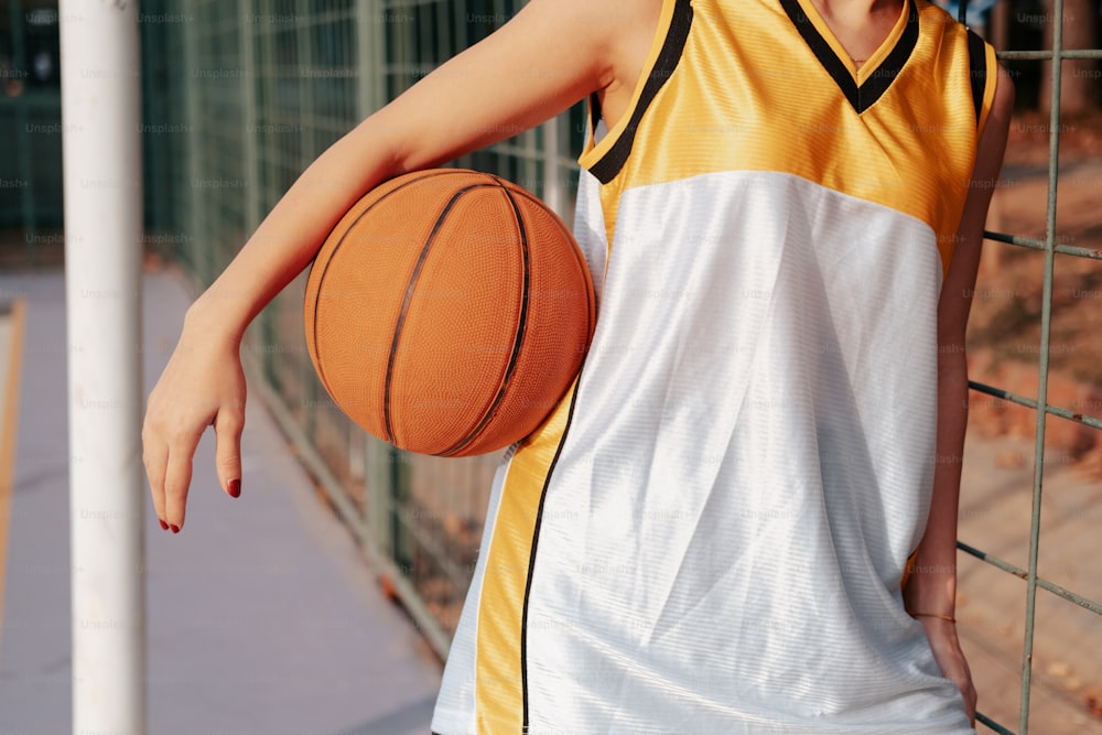 a woman holding a basketball standing next to a fence