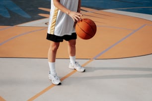 Un joven sosteniendo una pelota de baloncesto encima de una cancha de baloncesto