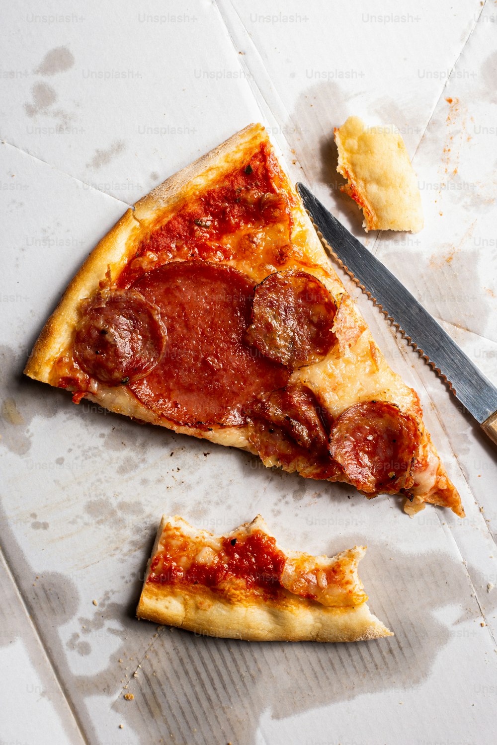 ein Stück Peperoni-Pizza, das auf einem Tisch neben einem Messer sitzt