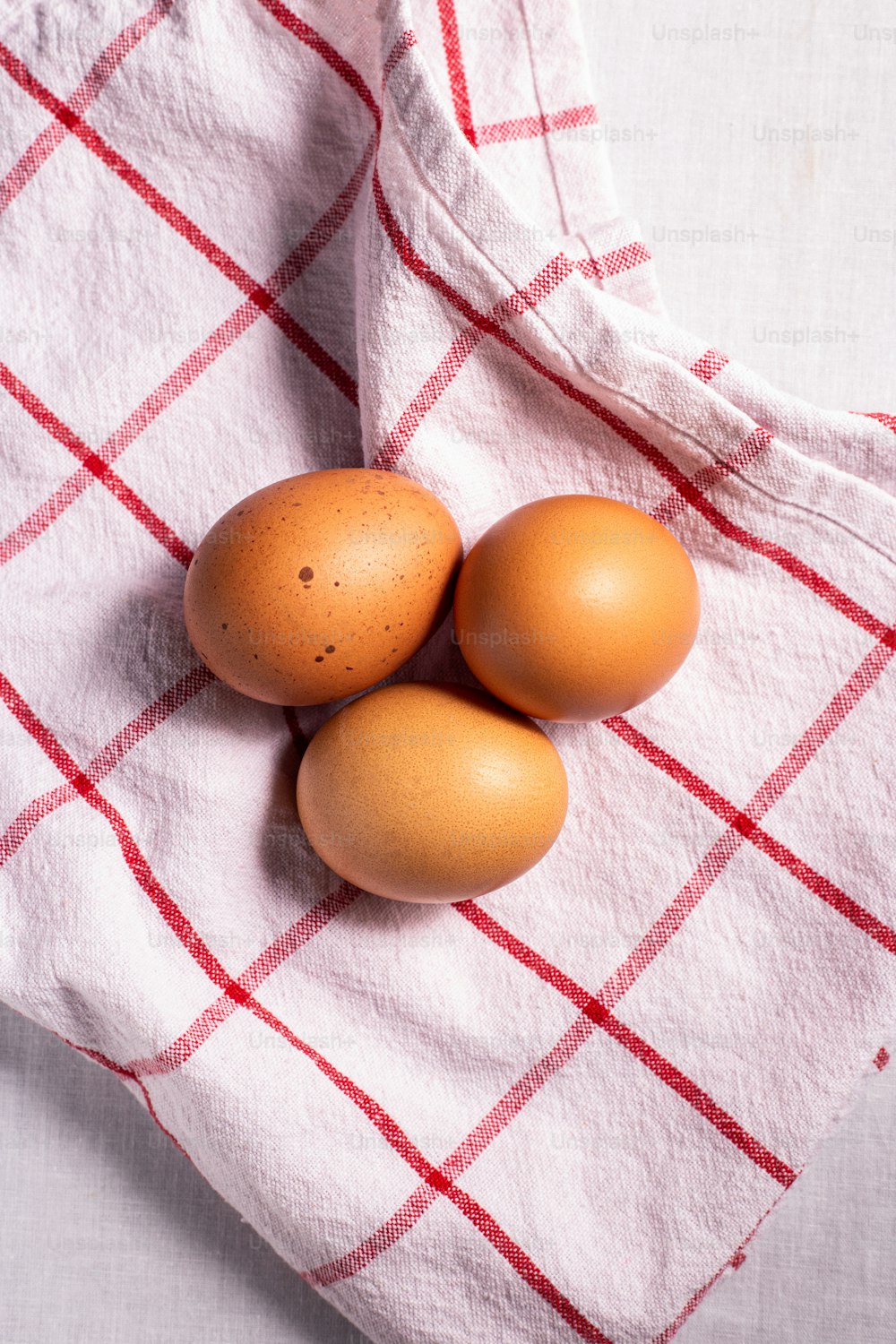 three brown eggs on a red and white checkered towel