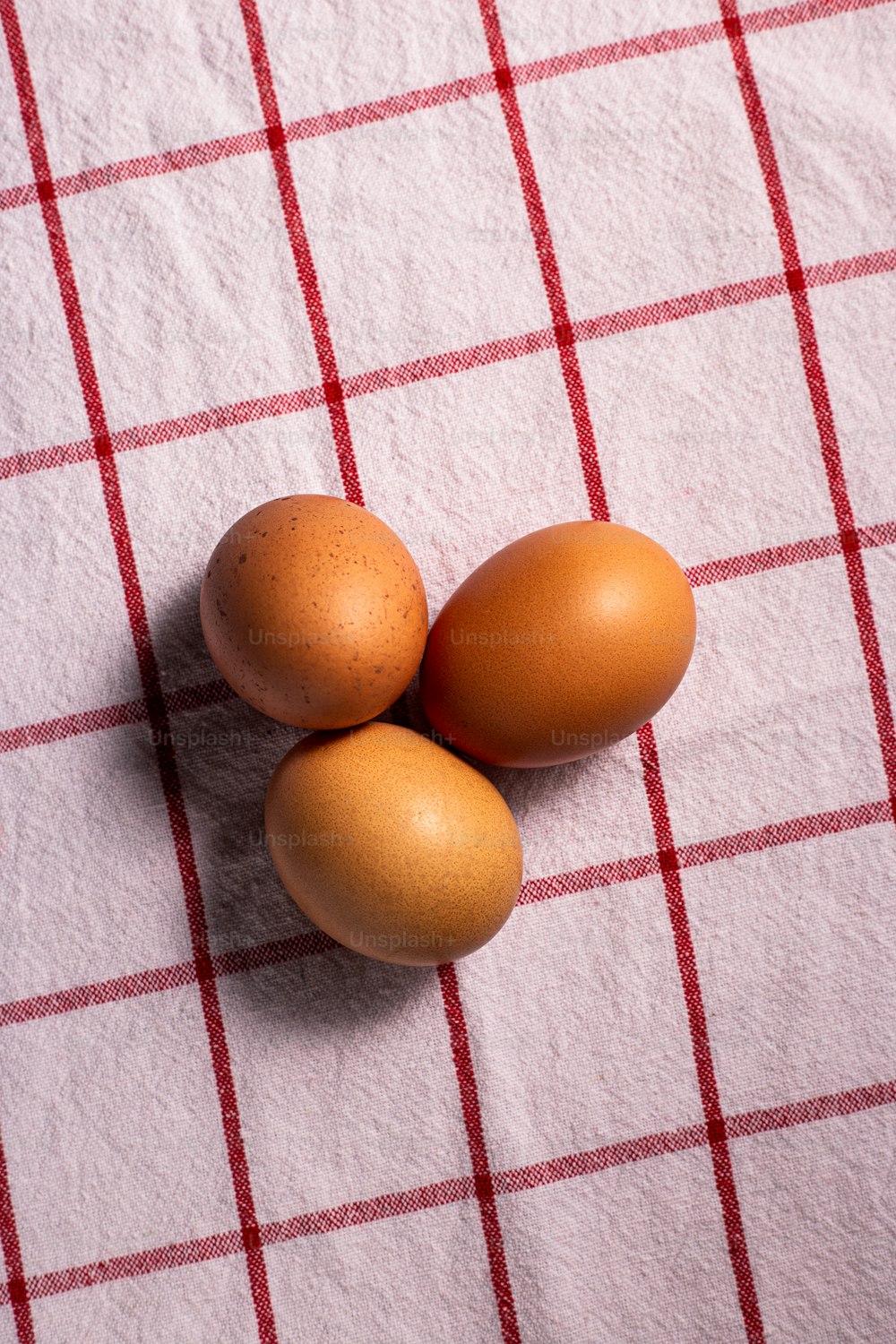 three brown eggs on a red and white checkered tablecloth