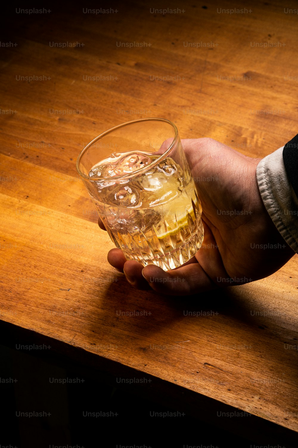 Una persona sosteniendo un vaso de alcohol en una mesa de madera